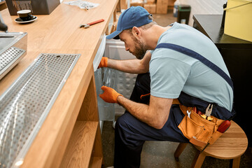 Canvas Print - Bearded young man repairing fridge in cafe