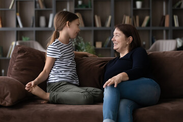 Wall Mural - Caring mature grandmother and little granddaughter talking, sitting on couch at home, happy senior woman with adorable girl child having fun, sharing secrets, telling news, enjoying leisure time