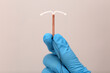 Doctor holding T-shaped intrauterine birth control device on grey background, closeup