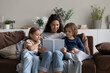 © fizkes - Smiling mother reading book to adorable little kids sitting on cozy couch at home, loving mom with little son and daughter engaged in educational activity, family spending leisure time together