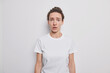 © WHstudio Leushin N - Waist up shot of worried woman with dark combed hair gasps from wonder hass puzzled expression dressed in casual t shirt poses against white background afraids of something trembles from fear