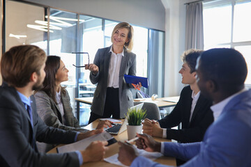 Canvas Print - Female boss addressing meeting around boardroom table.