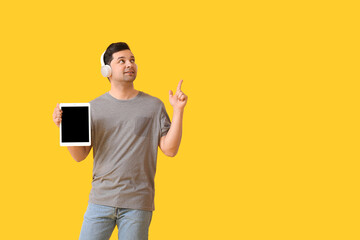 Wall Mural - Young man with tablet computer and headphones pointing at something on color background