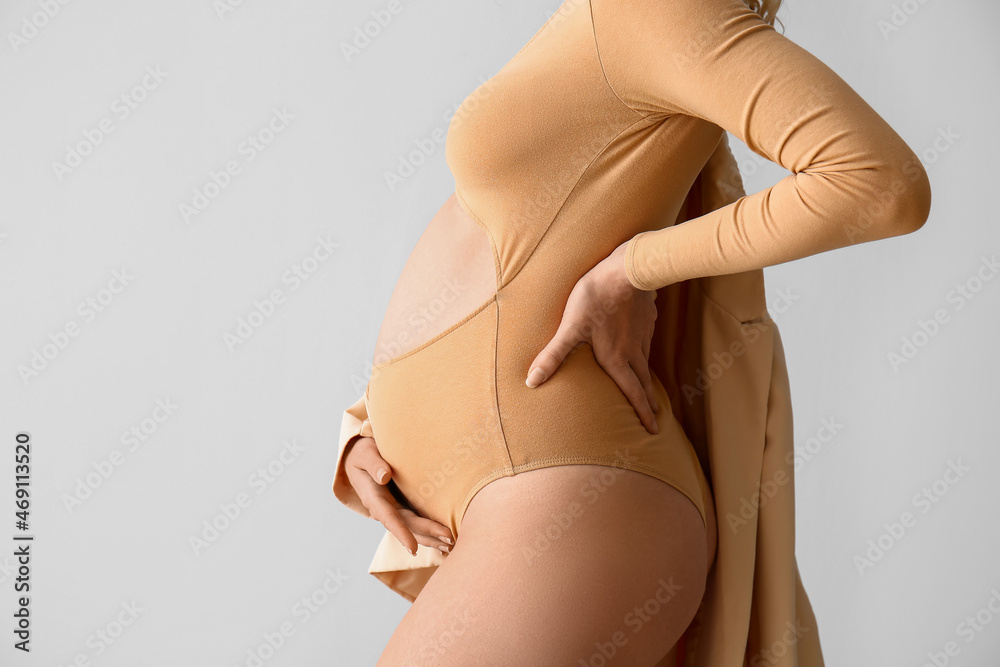 Stylish young pregnant woman on light background