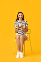 Canvas Print - Beautiful woman with cup of coffee sitting on chair against color background