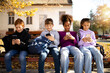 © littlewolf1989 - Group of multicultural children sitting on bench and using their smart phones surfing internet - technology concept.