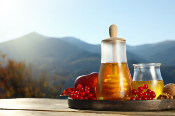 Fresh aromatic honey, rowan berries, apples and nuts on wooden table against mountain landscape. Space for text