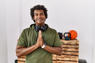 Wall Mural - African man with curly hair wearing sportswear at the gym begging and praying with hands together with hope expression on face very emotional and worried. begging.