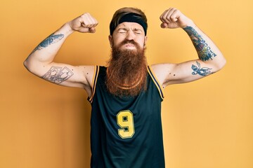 Wall Mural - Redhead man with long beard wearing basketball uniform showing muscles puffing cheeks with funny face. mouth inflated with air, catching air.