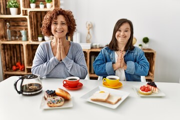 Poster - Family of mother and down syndrome daughter sitting at home eating breakfast praying with hands together asking for forgiveness smiling confident.