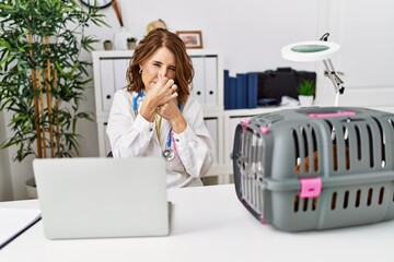 Canvas Print - Middle age veterinarian woman working at pet clinic smelling something stinky and disgusting, intolerable smell, holding breath with fingers on nose. bad smell