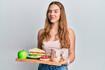 Canvas Print - Young blonde woman holding tray with breakfast food winking looking at the camera with sexy expression, cheerful and happy face.