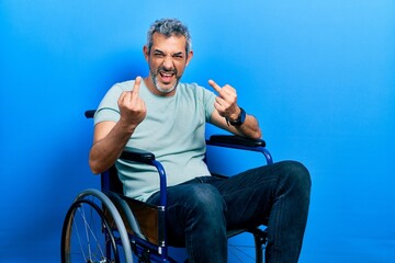 Canvas Print - Handsome middle age man with grey hair sitting on wheelchair showing middle finger doing fuck you bad expression, provocation and rude attitude. screaming excited