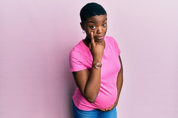 Poster - Young african american woman expecting a baby, touching pregnant belly pointing to the eye watching you gesture, suspicious expression