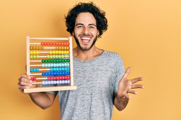 Sticker - Handsome hispanic man holding traditional abacus celebrating achievement with happy smile and winner expression with raised hand