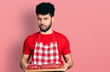 © Krakenimages.com - Young arab man with beard holding board with raw meat clueless and confused expression. doubt concept.