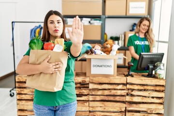 Sticker - Young brunette woman at wearing volunteer t shirt holding bag with food with open hand doing stop sign with serious and confident expression, defense gesture