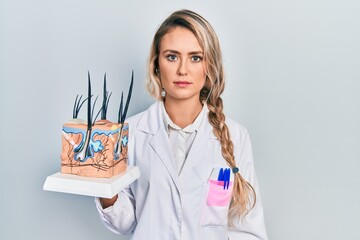 Poster - Beautiful young blonde woman holding model of anatomical skin and hair thinking attitude and sober expression looking self confident