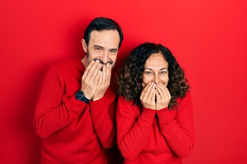 Sticker - Middle age couple of hispanic woman and man hugging and standing together laughing and embarrassed giggle covering mouth with hands, gossip and scandal concept