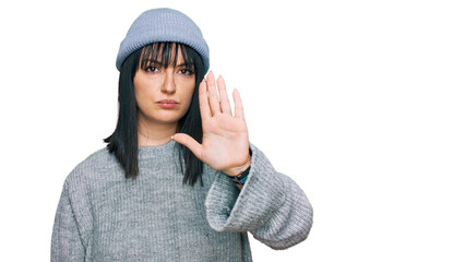 Sticker - Young hispanic woman wearing cute wool cap doing stop sing with palm of the hand. warning expression with negative and serious gesture on the face.