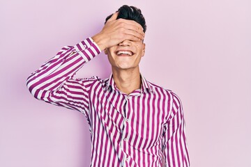 Wall Mural - Young hispanic man wearing casual clothes smiling and laughing with hand on face covering eyes for surprise. blind concept.