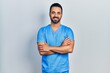 © Krakenimages.com - Handsome hispanic man with beard wearing blue male nurse uniform happy face smiling with crossed arms looking at the camera. positive person.