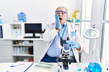 Canvas Print - Senior caucasian man working at scientist laboratory afraid and shocked, surprise and amazed expression with hands on face