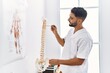 © Krakenimages.com - Young arab man wearing physiotherapist uniform pointing to vertebral column at clinic