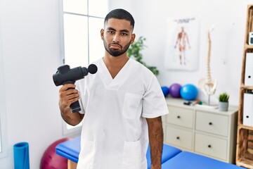 Sticker - Young indian physiotherapist holding therapy massage gun at wellness center depressed and worry for distress, crying angry and afraid. sad expression.