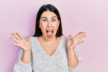 Wall Mural - Young hispanic woman wearing casual clothes celebrating crazy and amazed for success with arms raised and open eyes screaming excited. winner concept