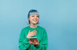 © bodnarphoto - Happy girl with colored hair and makeup stands with a smartphone in his hands on a blue background and looks away with a smile on his face.