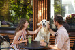 © Seventyfour - Portrait of happy couple with dog sitting at table together in outdoor cafe and laughing, copy space