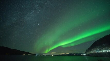 bright lights of the aurora borealis above the sea. cars with bright headlights pass on the coastal 