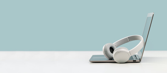 laptop. mockup screen and wireless headphones on white desk. plain blue background. distant learning