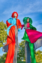 Positive Stilt Walkers In Multicolored Costumes Standing Together In Park