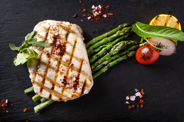 Wall Mural - White fish steak with vegetables on balck stone. Top view