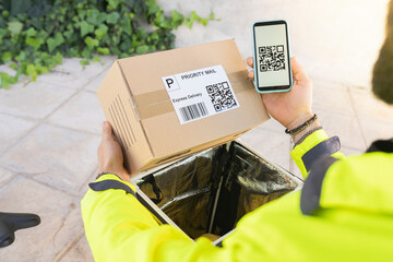 Delivery man with mobile phone holding package in public park