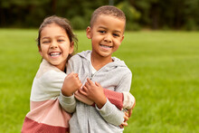 Childhood, Leisure And People Concept - Happy Smiling Little Boy And Girl Hugging At Park