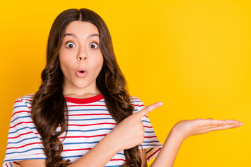 Sticker - Photo of young shocked amazed surprised girl demonstrating product advertisement isolated on yellow color background