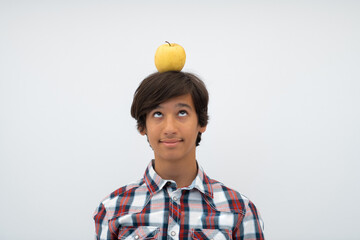 Wall Mural - A funny portrait of a young attractive Arab boy with apple on his head isolated on a white background. Selective focus 