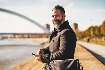 Businessman is sitting outdoor in the city and using smartphone.