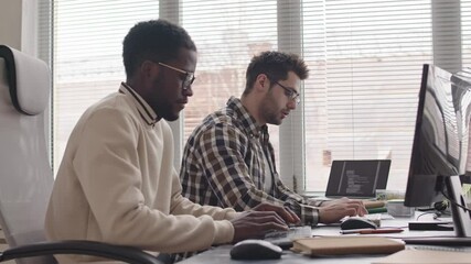 Wall Mural - side-view medium slowmo shot of two young multi-ethnic male programmers developing new software sitt