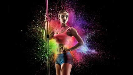 Wall Mural - Creative portrait of young female athlete, sportive woman standing in explosion of colored neon powder isolated on dark background