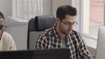 Wall Mural - panning chest-up shot of two young multi-ethnic programmers sitting in front of computer monitors in