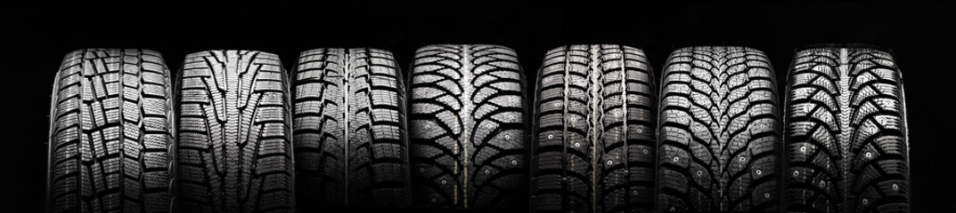 Wall Mural - a lot of winter studded tires and velcro tires stand in a row on a black background panorama