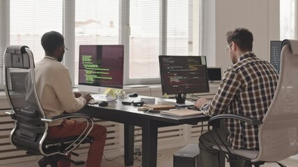 Wall Mural - rear-view slowmo stab shot of two male software developers or engineers writing program codes on pc 