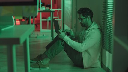 Wall Mural - stab shot of male programmer in casualwear and eyeglasses sitting on floor in office with green and 