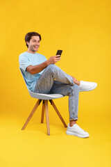 Poster - Happy guy using cell phone at studio, sitting on chair