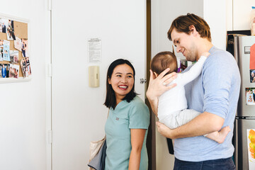 Smiling Woman coming home and  looking At Daughter Held By Husband