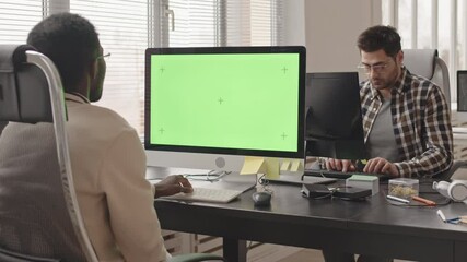 Wall Mural - slowmo stab shot of two young multiethnic software developers sitting at workplaces in contemporary 